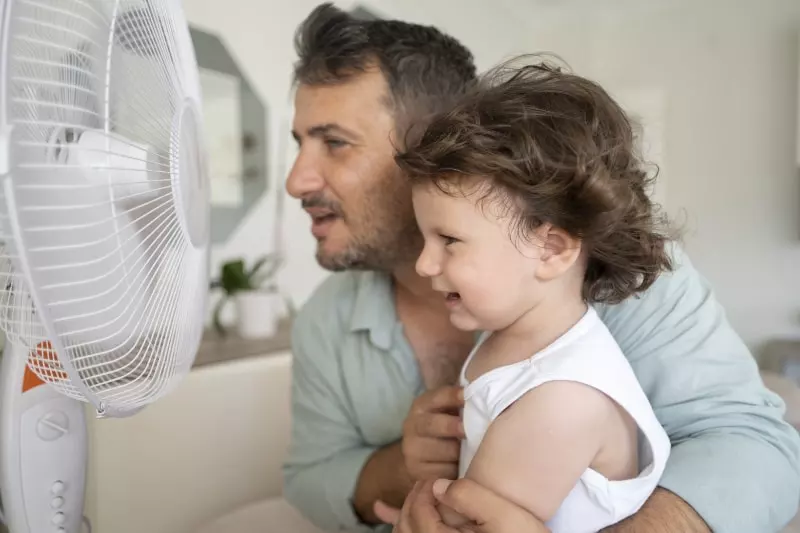 Father and young daughter trying to stay cool by sitting in front of a fan 