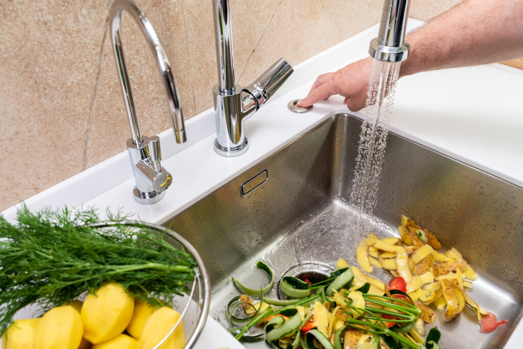 Person washing food waste into a stainless steel kitchen sink drain with a garbage disposal.