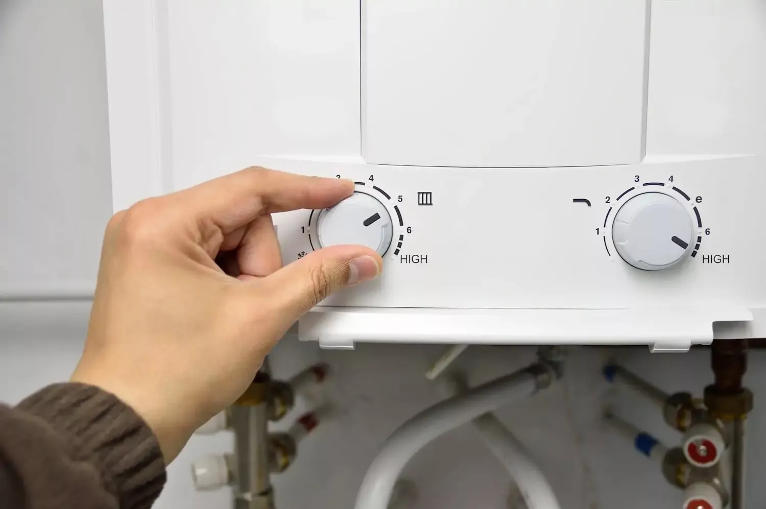  A hand adjusting a knob on a tankless water heater. 