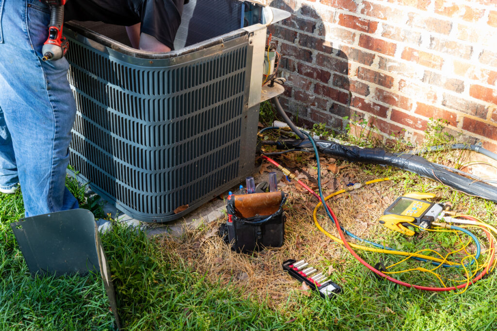 Air conditioner maintenance being performed by a technician, next to a brick home.