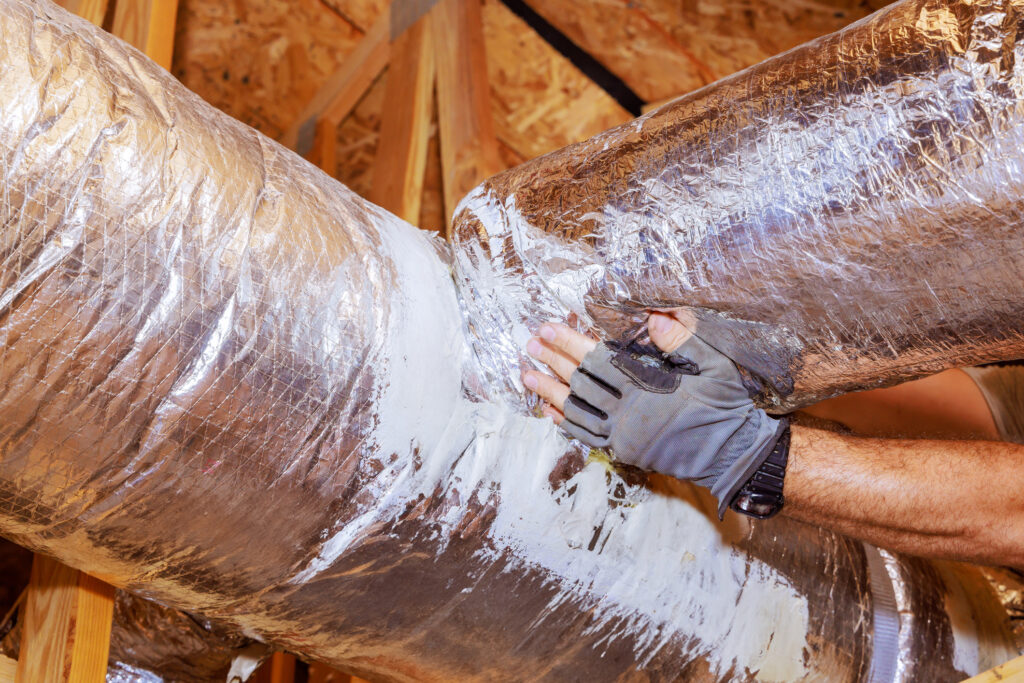 Close view of a technician's hand as they perform ductwork repairs in the attic of a home.
