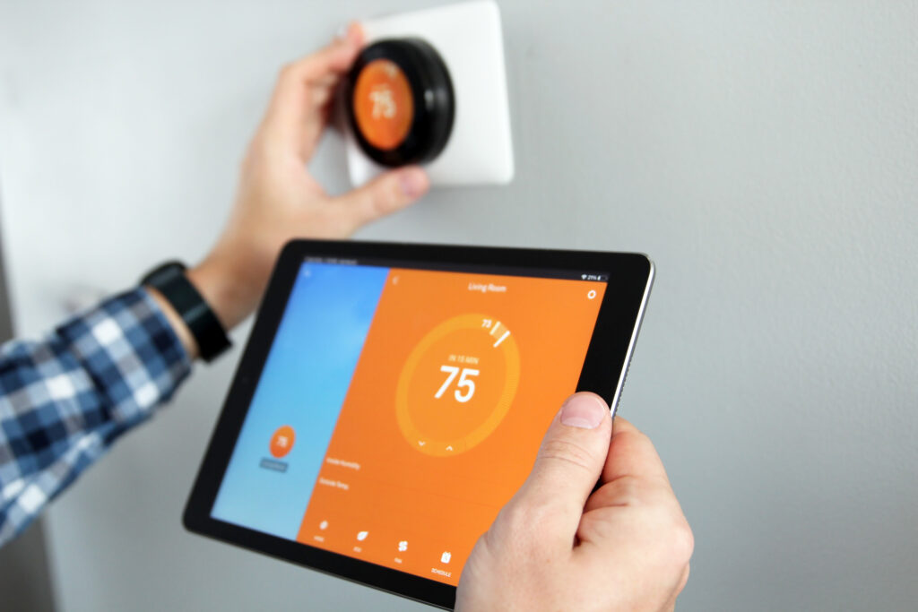 A person adjusting the temperature using a tablet with smart home app in modern living room, while adjusting smart thermostat on the wall, blurred in background.